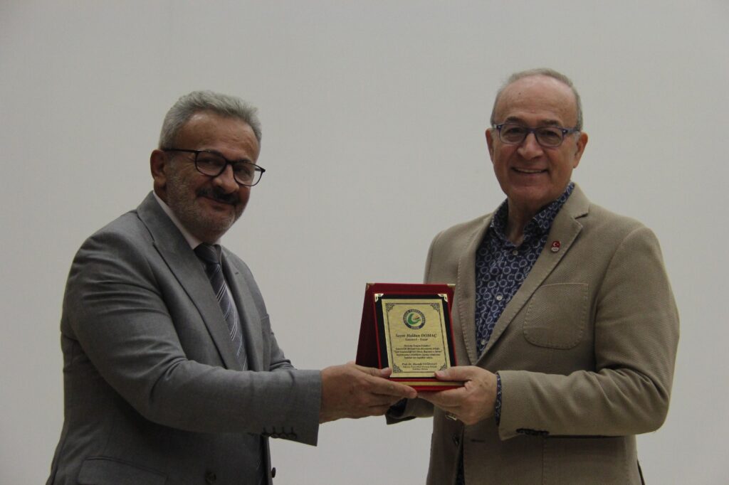 Söyleyişinin ardından Prof. Dr. Mustafa Yağbasan, katkılarından dolayı Haldun Domaç'a teşekkür plaketi takdim ederken.
